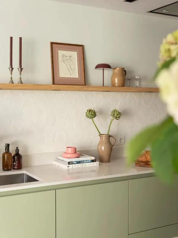 Keuken met witte zeshoekige Hexa White-wandtegels, lichtgroene kastjes, een houten plank en roze accessoires.