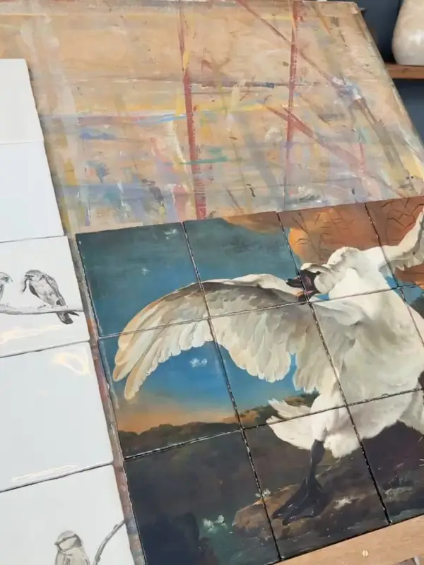 Tegeltableau met een witte zwaan met uitgespreide vleugels, naast witte tegels met vogeltekeningen.