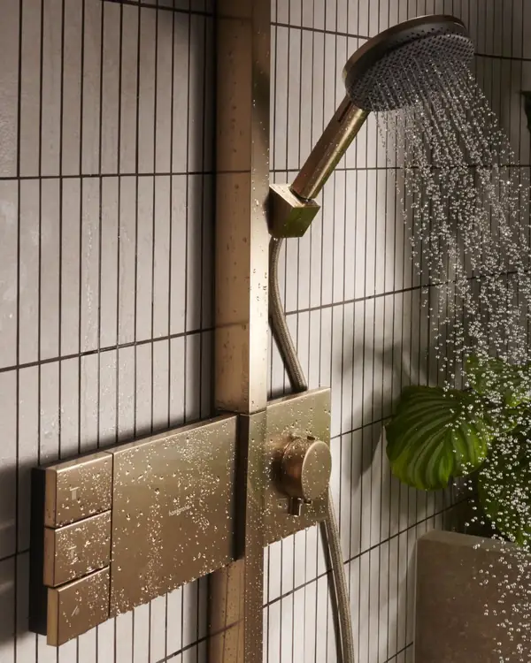 Hansgrohe handdouche in een warme metaaltint met stromend water, verticale wandtegels en een groen blad.