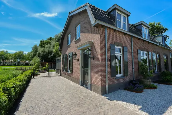 Bestrating in visgraat naast een bakstenen woning, met licht grind en cortenstalen borders bij Steenplaza LEXMOND