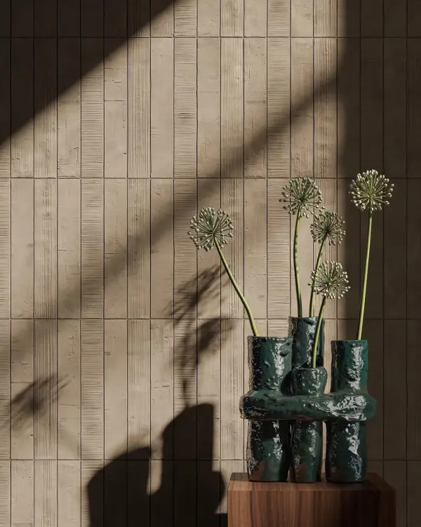 Beige Kore-wandtegels met afwisselend reliëf, naast een donkergroene vaas met bloemstelen op een houten sokkel.