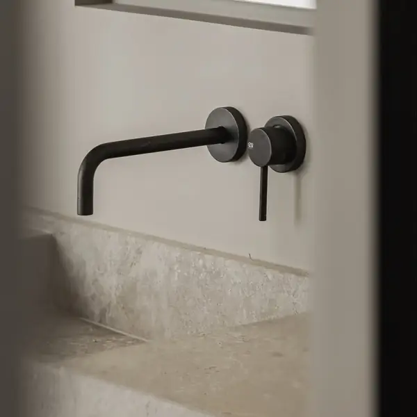 Donkere wandkraan boven een beige wastafel met wolkachtige tekening en een opstaande achterrand.