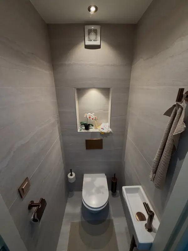 Grijze wandtegels met golvende tekening en verlichte toiletnis bij Yuvam Bouwmaterialen in Rotterdam